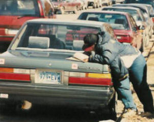 A very focused woman is filling out the survey on her car.